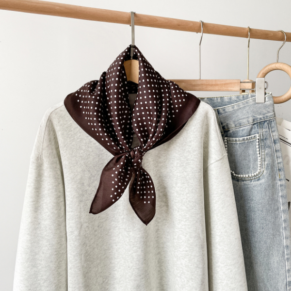 Brown polka dot scarf draped over a white shirt and jeans on a rack.