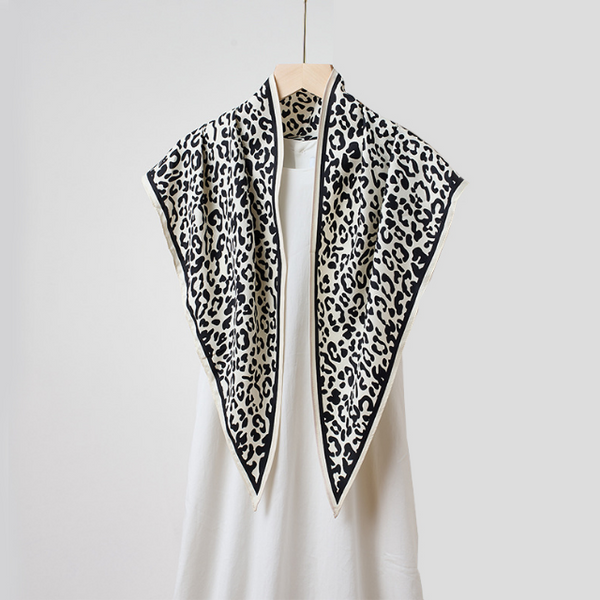 A black and white leopard print scarf draped over a white top on a wooden hanger against a light gray background.