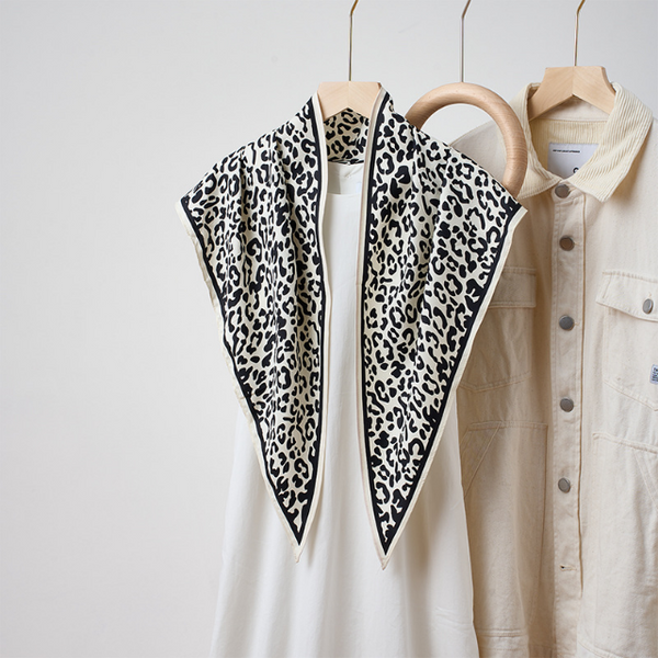 A black and white leopard print scarf draped over a white top on a wooden hanger against a light gray background.