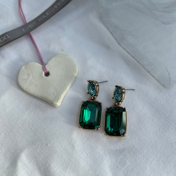 Green gemstone earrings on a white surface with a heart-shaped object and pink string.