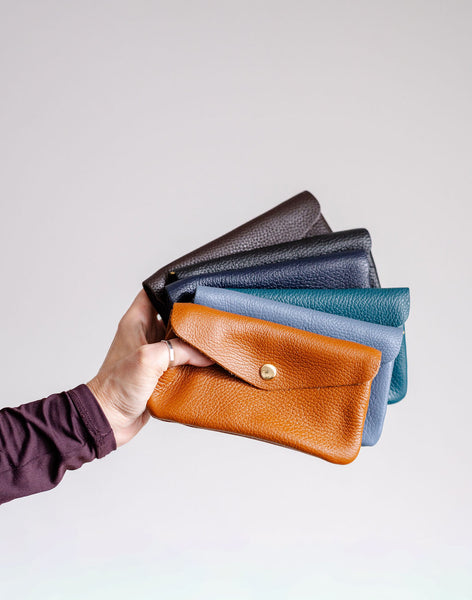 Hand holding a set of leather wallets in various colors on a light background