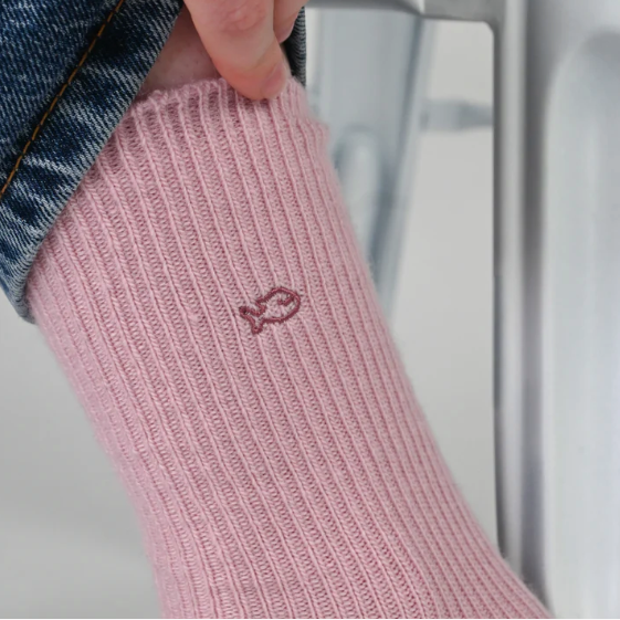 Pink sock with a small logo worn by a women in blue jeans, against a neutral background