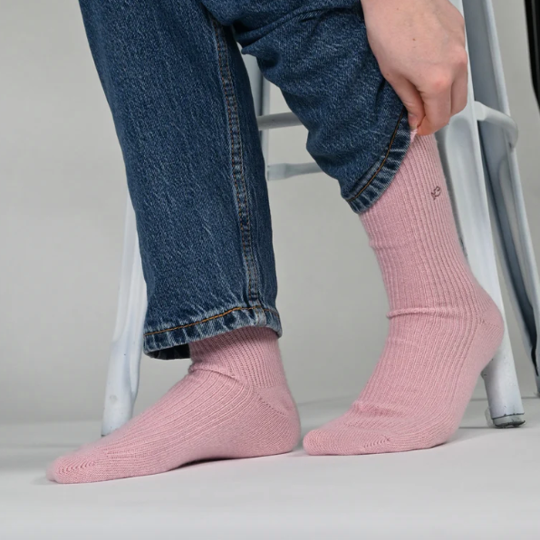 Person wearing pink socks and blue jeans sitting on a white chair.