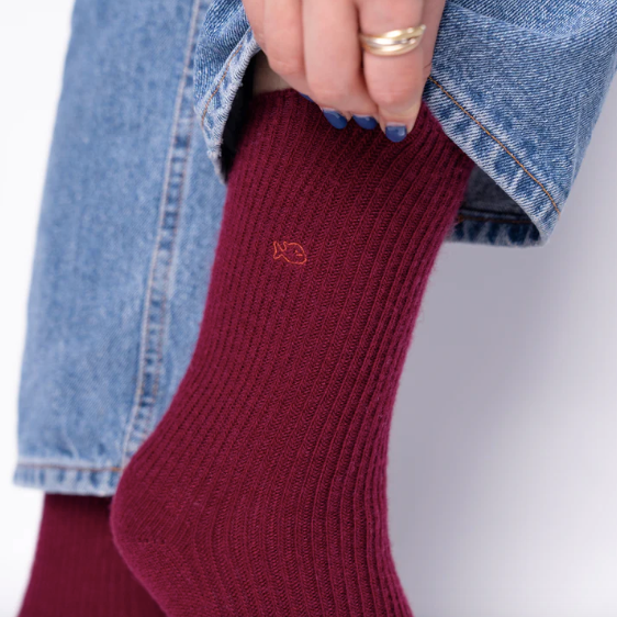 woman wearing a burgundy sock with a small logo, holding their jeans up