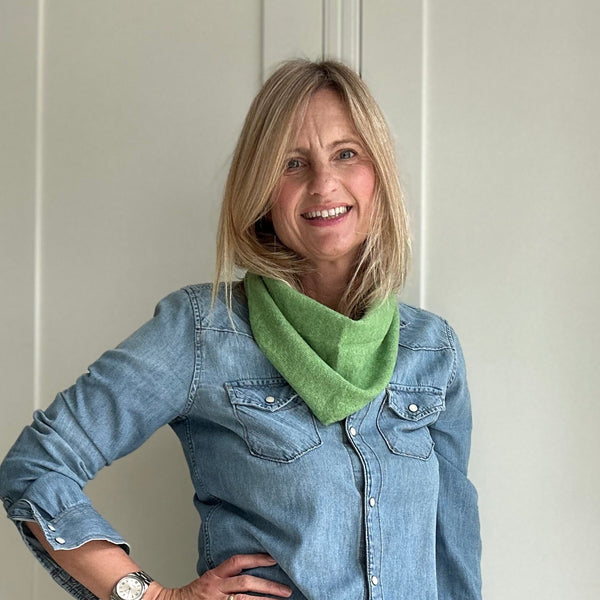 Woman wearing a denim shirt and green scarf standing indoors.