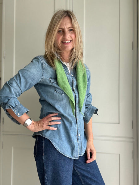 Woman wearing a blue denim shirt with rolled-up sleeves and a green scarf, standing indoors.