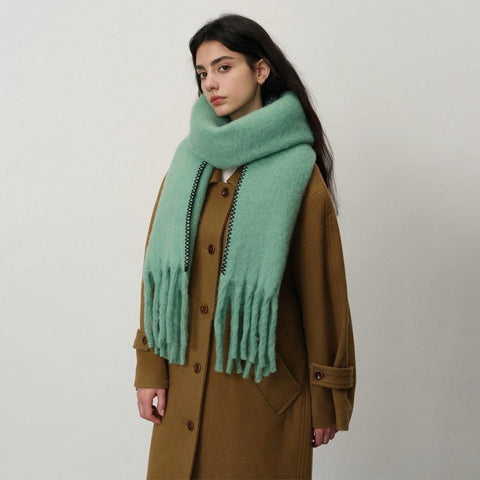 women in a camel coat with aqua green blanket scarf and stitch detail against a white background.