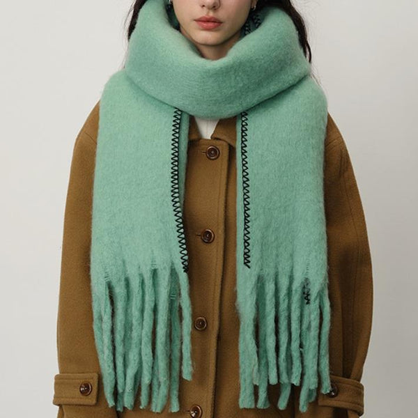 women in a camel coat with aqua green blanket scarf and stitch detail against a white background.