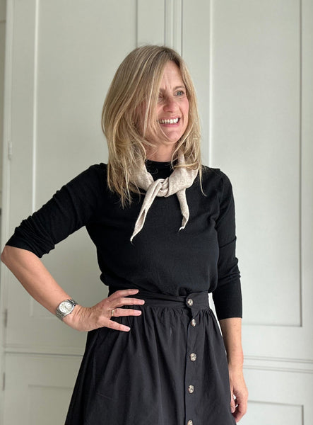 Woman wearing a black outfit with a beige scarf indoors
