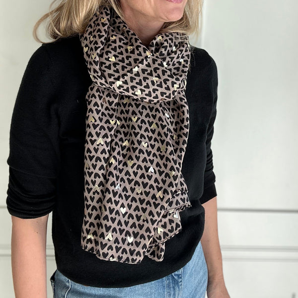 Woman wearing a heart print scarf in front of a white door.