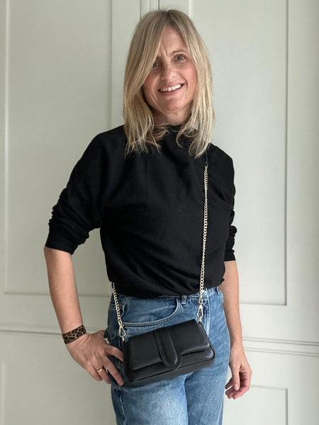 Woman holding a black handbag against a white door background