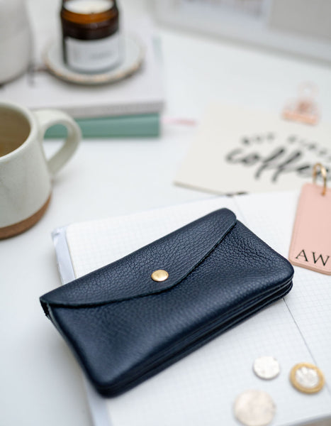 Black leather wallet on a white surface with a cup of coffee and other items.