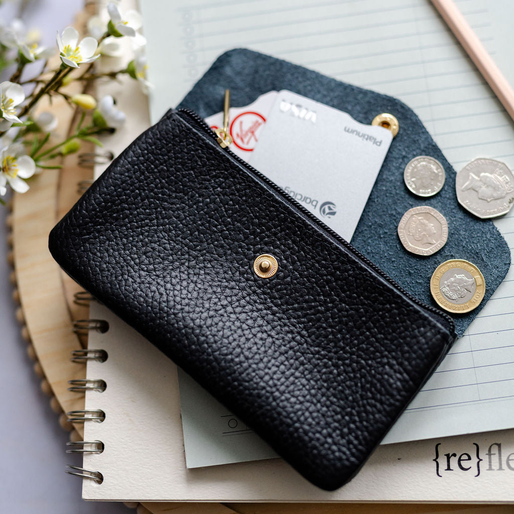 Black leather wallet with coins and cards on a notebook with flowers and pen in the background