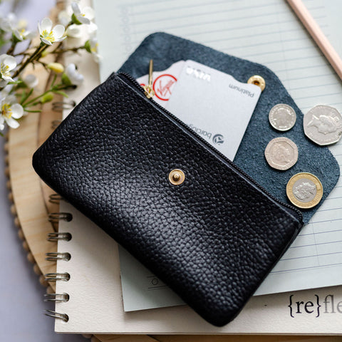 Black leather wallet with coins and cards on a notebook with flowers and pen in the background