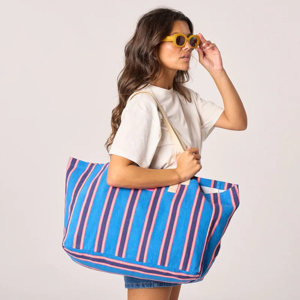 Woman holding a blue and pink striped tote bag against a plain background