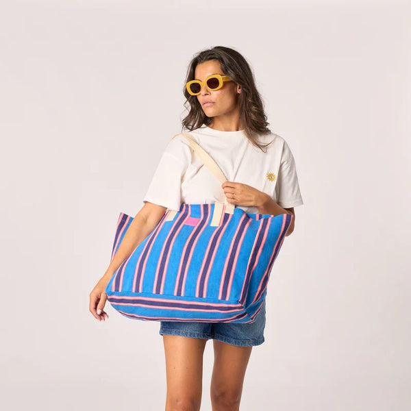Woman holding a large blue and pink striped bag against a white background
