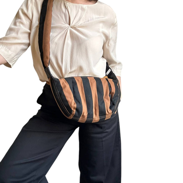 A person wearing a cream satin blouse and dark wide-leg pants carries a slouchy shoulder bag with vertical black and tan stripes against a plain white background.