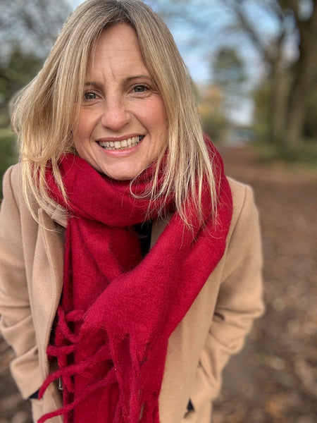 Woman wearing a red scarf and beige coat outdoors with trees in the background