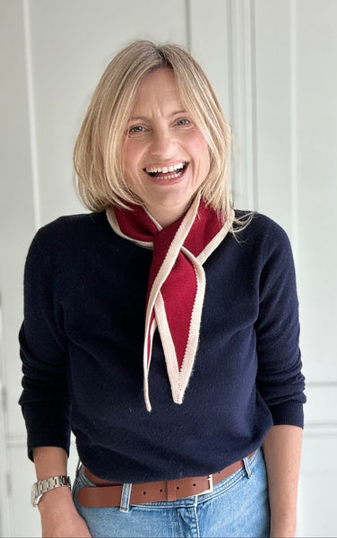 Woman wearing a navy sweater with a red scarf against a white paneled wall