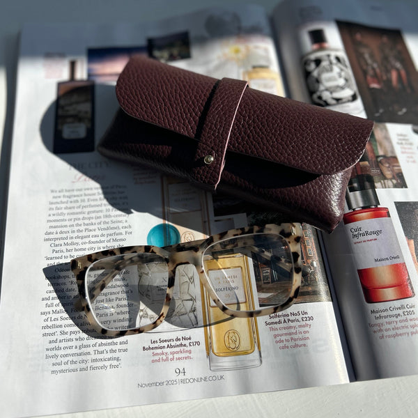 burgundy leather sunglasses case on a magazine with tortoiseshell glasses 