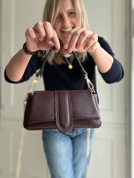 Woman holding a burgundy leather handbag in front of her face against a neutral background