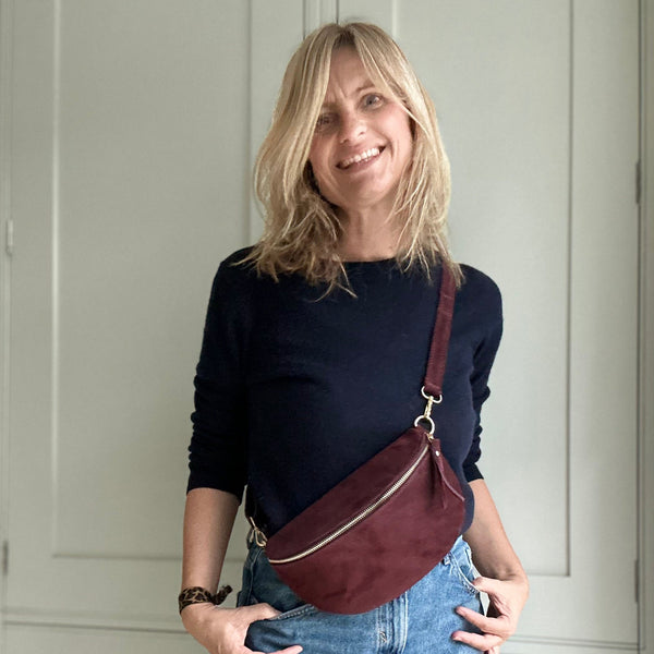 Woman wearing a dark blue sweater and jeans, carrying a burgundy leather bag indoors.