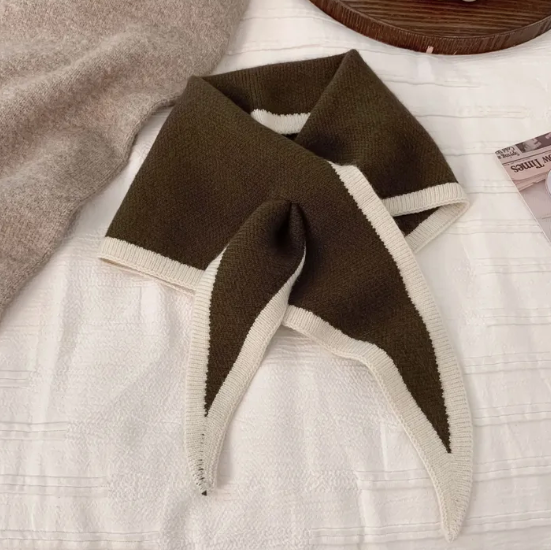 Brown and beige scarf on a white surface with a wooden plate and grapes in the background