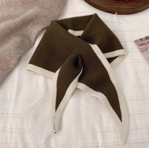 Brown and beige scarf on a white surface with a wooden plate and grapes in the background