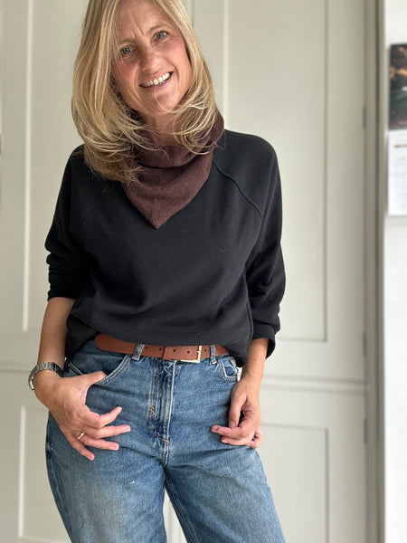 Woman wearing a black sweater with a brown scarf and blue jeans indoors.