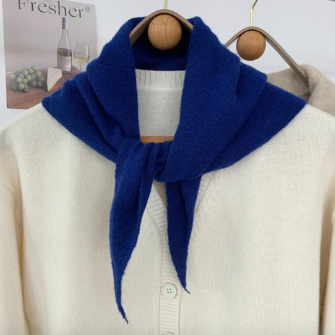 Cobalt blue skinny triangle knit wool scarf draped over a beige sweater on a wooden hanger against a white background.