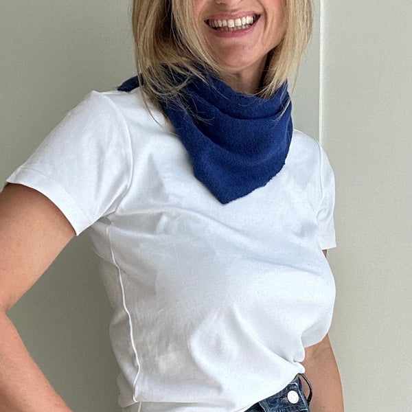 Woman wearing a white t-shirt, blue jeans, and a blue scarf standing against a neutral wall.
