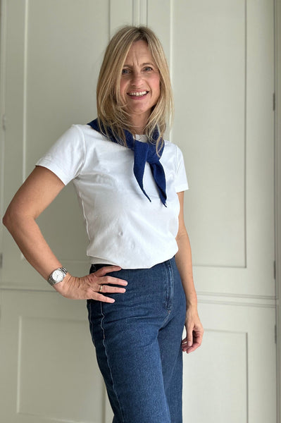 Woman wearing a white shirt with a blue scarf and jeans, standing indoors.