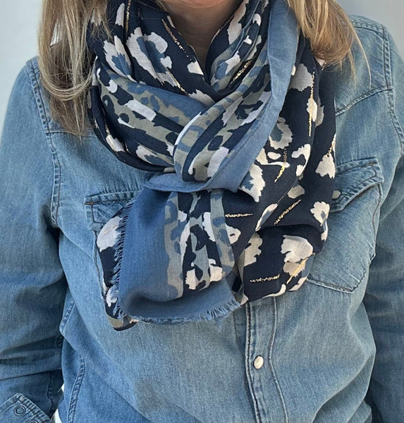 Woman wearing a denim jacket and leopard print scarf against a white wall