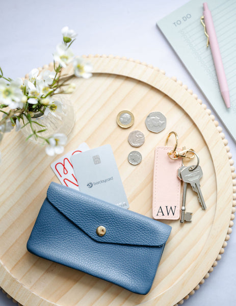 Blue wallet with cards, coins, keys, and a tag on a wooden tray with flowers and stationery.