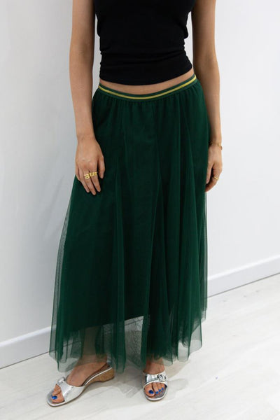 woman wearing a deep green floaty skirt and a black top with silver shoes against a white background