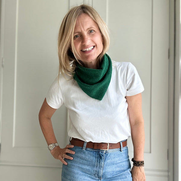 Woman wearing a white t-shirt, green scarf, and blue jeans against a white wall.