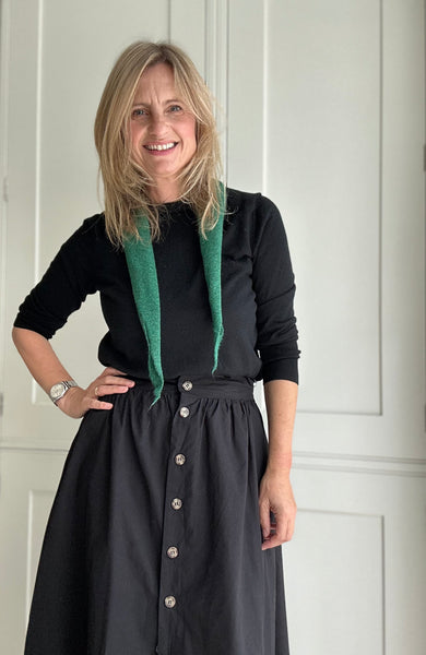 woman in black skirt and sweater with a forest green rolled scarf