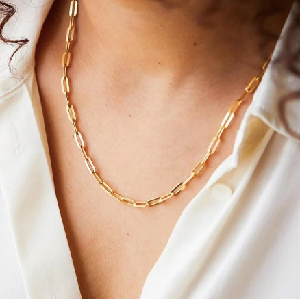 A close-up of a gold paperclip chain necklace worn by a person in a white collared shirt.