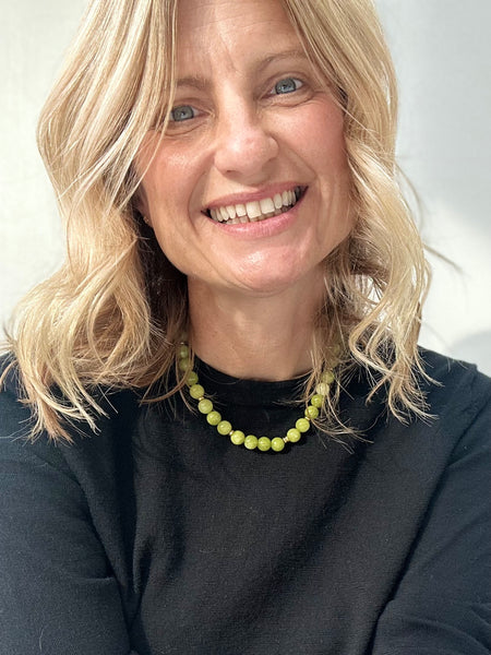 Woman with blonde hair wearing a black top and green quartz necklace against a white background