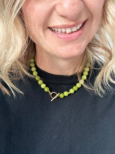 woman wearing a green beaded necklace with a gold t-bar clasp on a black shirt.