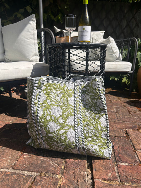 Cotton bag with green floral pattern on a patio with outdoor furniture and wine bottle.