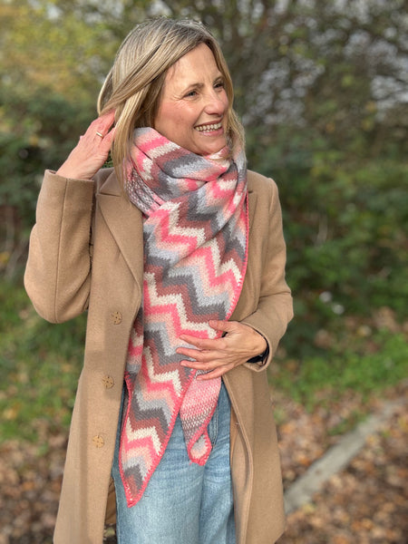 Woman wearing a beige coat and a colorful zigzag scarf outdoors.