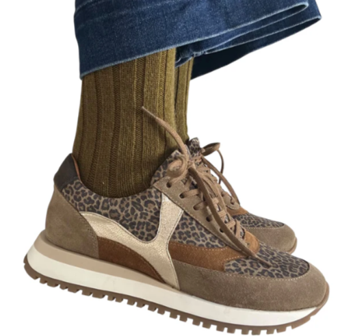 Brown and beige patterned sneakers worn with green socks and blue jeans on a white background