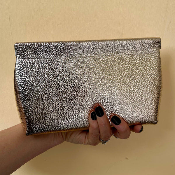 Gold leather clutch held by a hand against a beige background