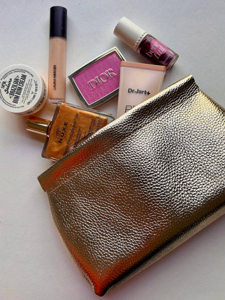 Gold leather clutch with makeup products including a Dior palette and various bottles.
