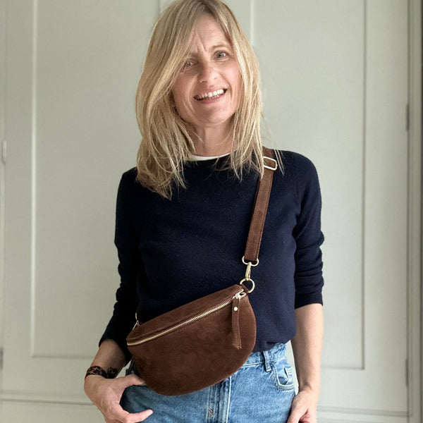 Woman wearing a navy sweater and blue jeans with a brown leather bag in a neutral setting.