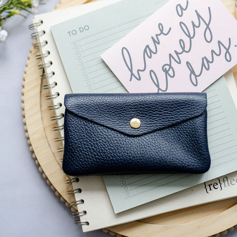 Navy blue leather wallet on a notebook with a card reading 'Have a lovely day' on a light gray background.