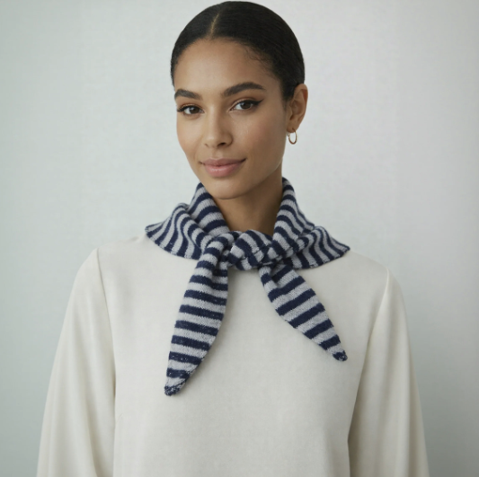 Woman wearing a white sweater and a blue and white striped scarf against a plain background