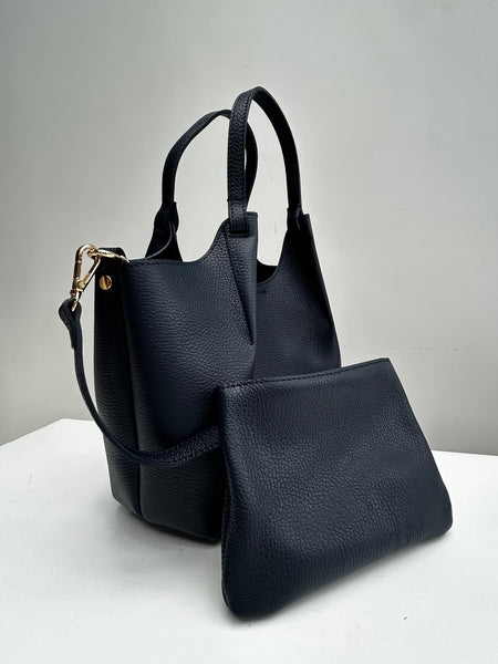 navy blue leather bag with top handles and an inner leather pouch on a white table
