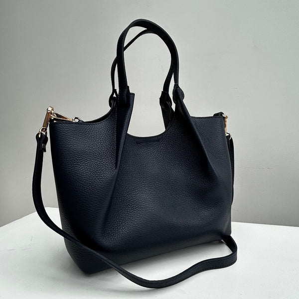 navy leather bag with top handles and a slim strap on a white table